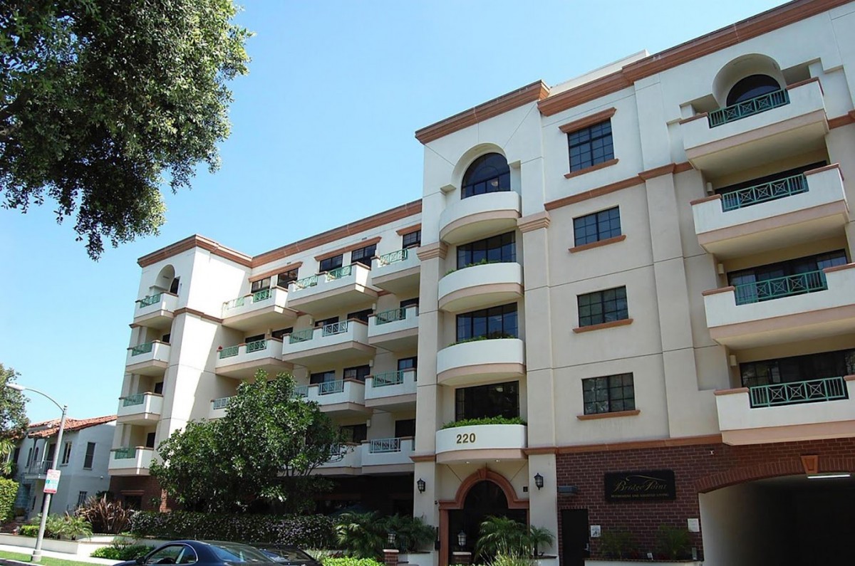 A multi-story residential apartment building with balconies and surrounding trees.
