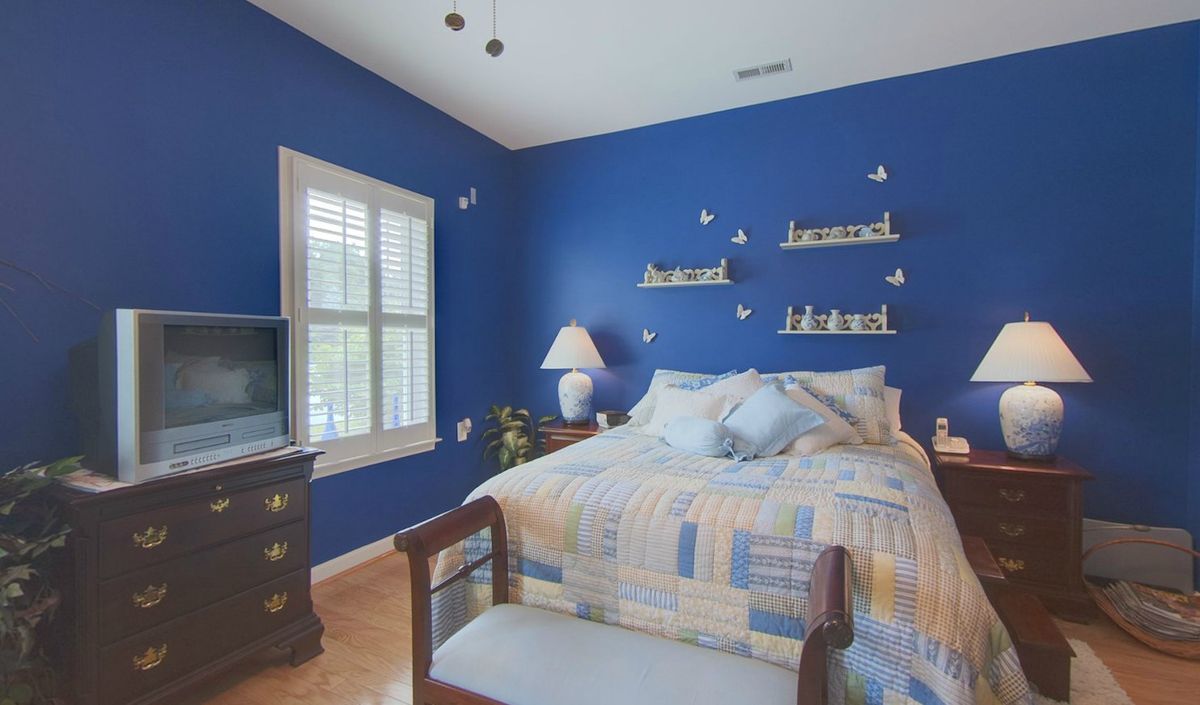 A cozy bedroom with blue walls, featuring a bed and decorative shelves.