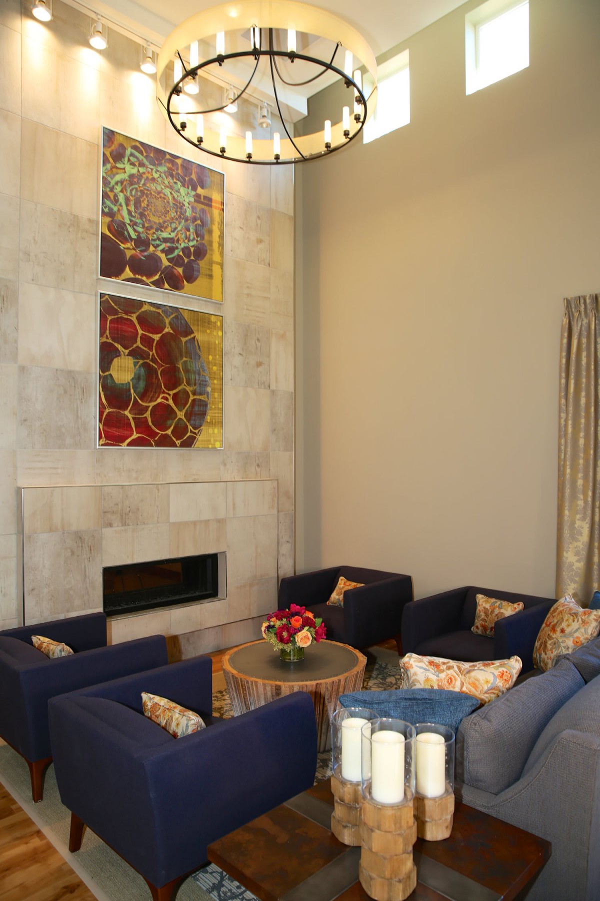 A modern living room with blue armchairs, a fireplace, and abstract artwork.