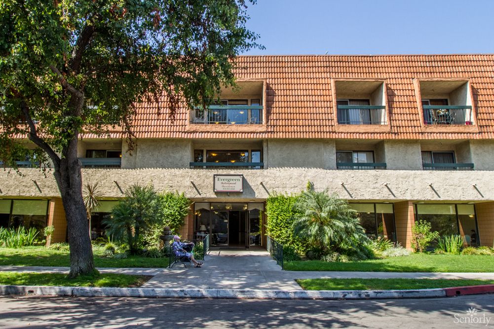 A multi-story building with a brick facade and a lush green entrance.