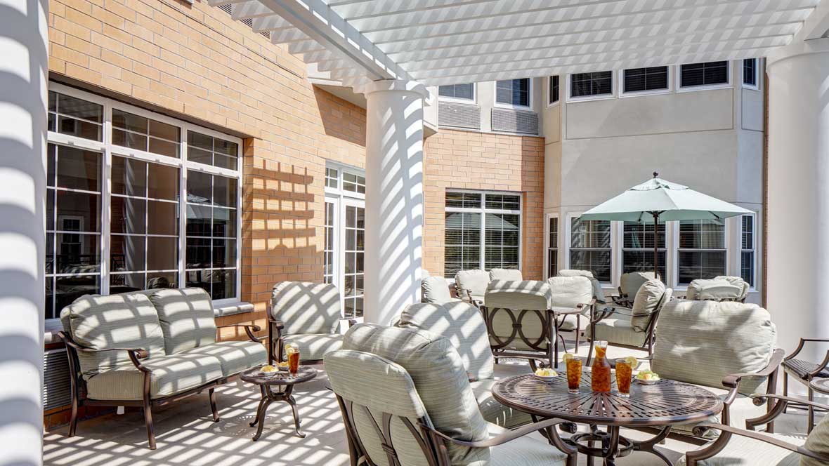 A sunny outdoor patio with comfortable seating and tables under a pergola.