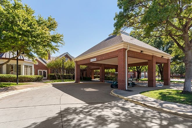 A building entrance with a covered driveway surrounded by trees on a sunny day.
