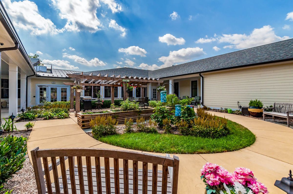 A beautiful courtyard garden with pathways, vibrant flowers, and a pergola under a clear blue sky.