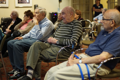 A group of elderly men seated, engaged in a gathering at a community center.