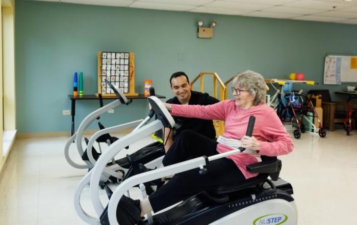An elderly woman engaging in physical therapy with the assistance of a trainer, using exercise equipment.