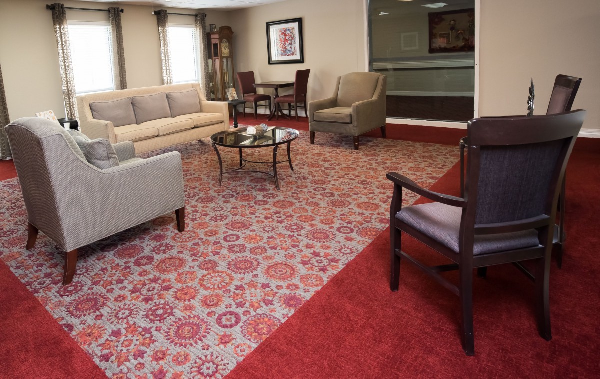 A cozy lounge area with a patterned carpet, multiple chairs, and a sofa arranged around a glass coffee table.
