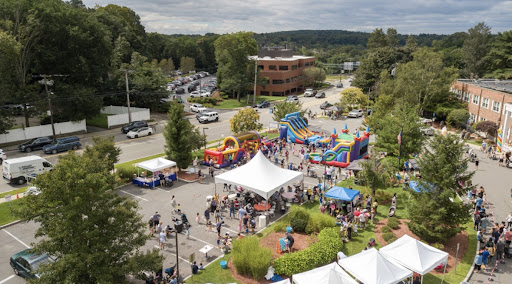A bustling outdoor community event featuring various attractions, including bouncy castles and food tents.