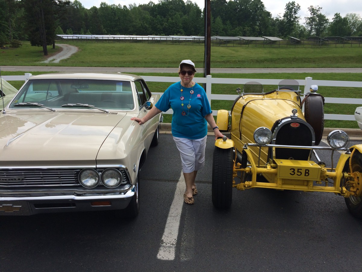 A woman stands between a classic and a vintage car parked outdoors.