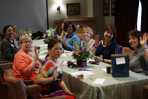 A group of women enjoying a lively gathering, smiling and waving at the camera.