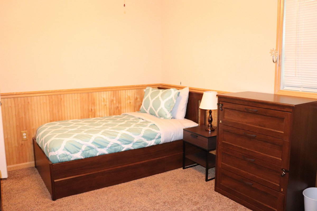 A cozy single bedroom with a wooden dresser and nightstand.