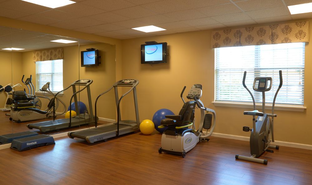 A small gym with treadmills and an exercise bike, featuring a TV and fitness balls.