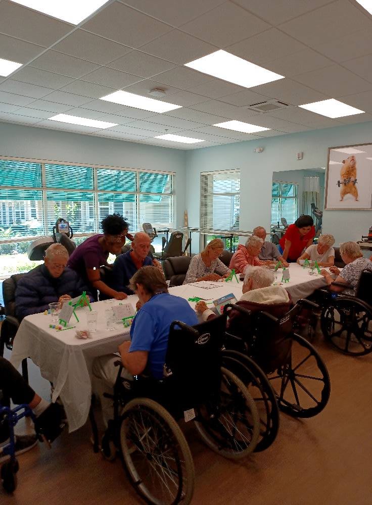 A group of elderly people in wheelchairs gathered around a table in a nursing home setting.