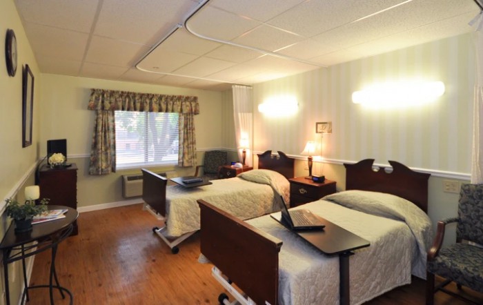 A nursing home room with two beds and warm lighting.