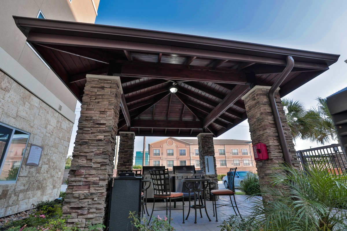 An outdoor gazebo with stone pillars and patio furniture, providing a shaded seating area.