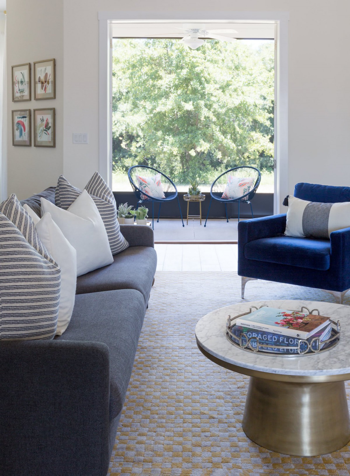A modern living room with a stylish blue armchair, striped pillows on a dark sofa, and a round coffee table overlooking an outdoor patio.
