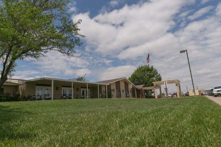 A building with a well-maintained lawn, trees, and an American flag against a partly cloudy sky.