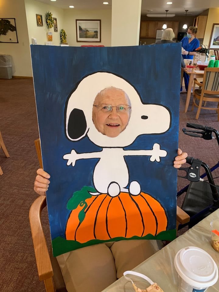 A person playfully poses with a Snoopy cutout, featuring the character on a pumpkin.