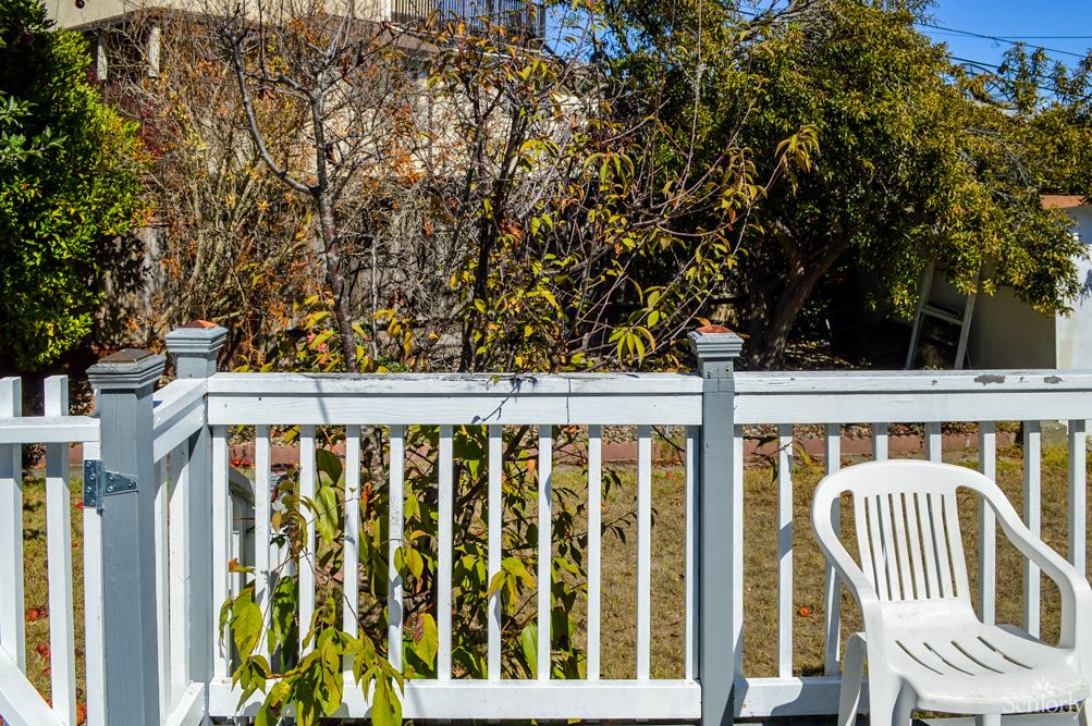 A patio deck with a white railing and chair, surrounded by trees and garden.