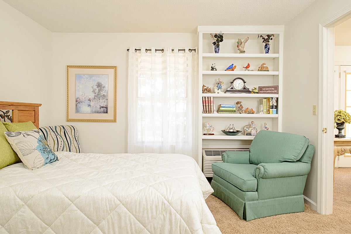 A cozy bedroom with a white bookshelf and a green armchair.