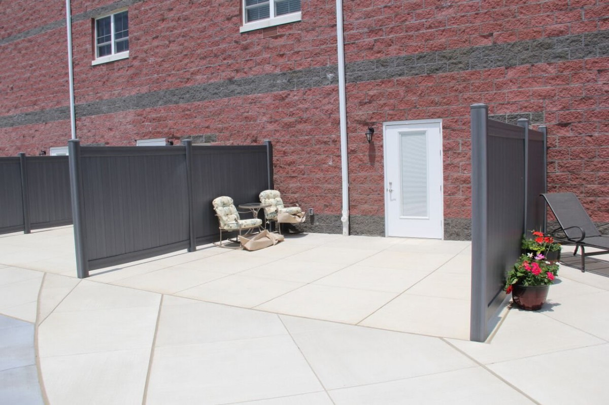 A small patio area with two chairs, surrounded by a brick building and privacy fencing.
