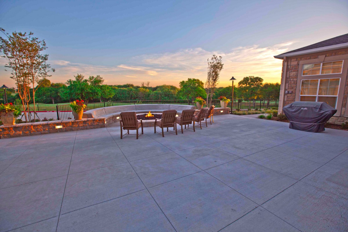 A spacious patio with outdoor seating and a fire pit overlooking a serene landscape at sunset.