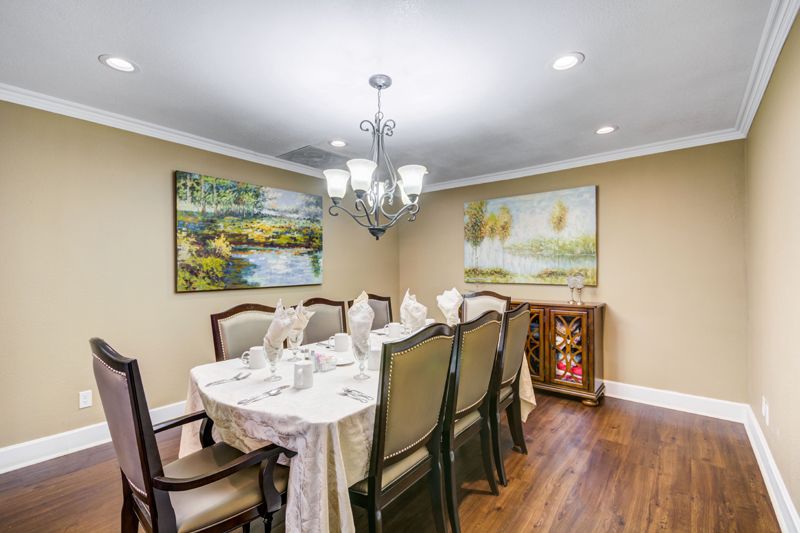 A well-decorated dining room with a chandelier, artwork on the walls, and a set dining table.