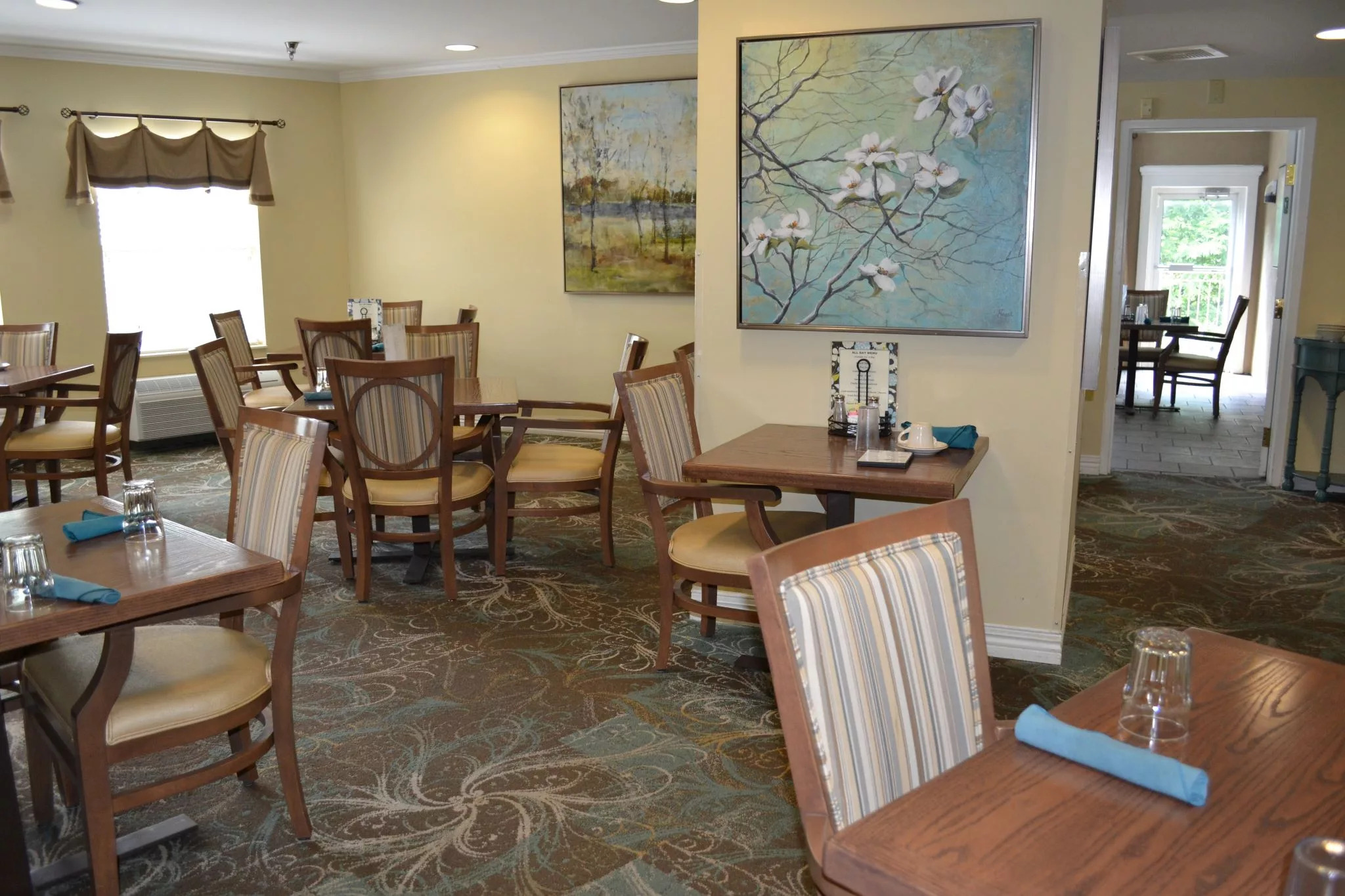 A cozy dining room with wooden tables and chairs, decorated with paintings on the walls.