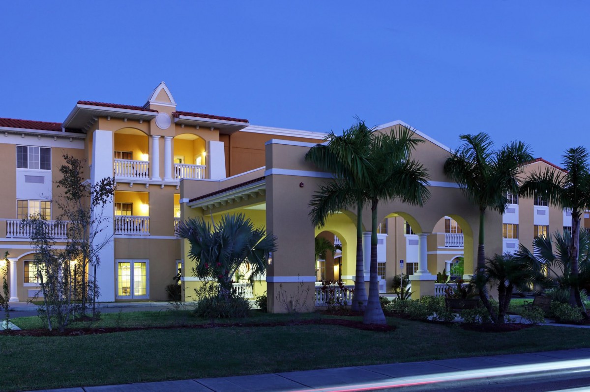 An illuminated residential building with palm trees at night.