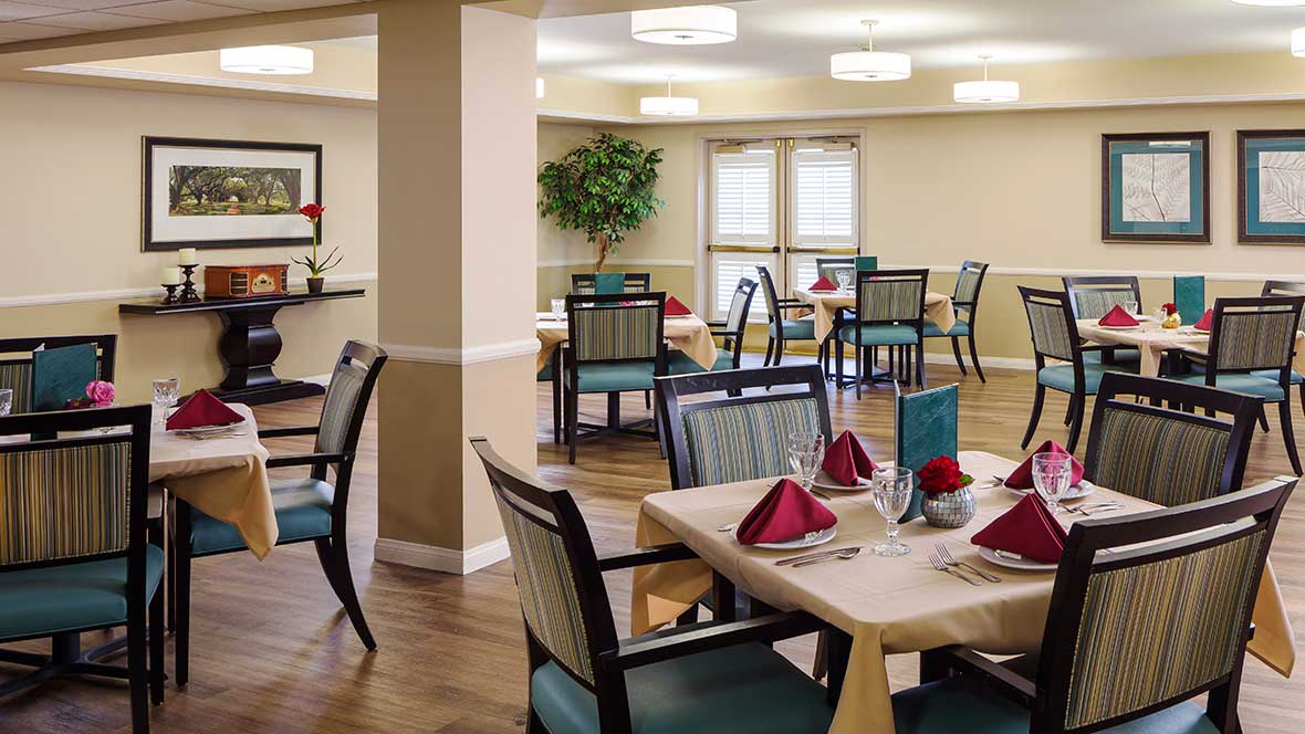 A cozy dining room setup with neatly arranged tables and chairs, featuring folded napkins and elegant lighting.
