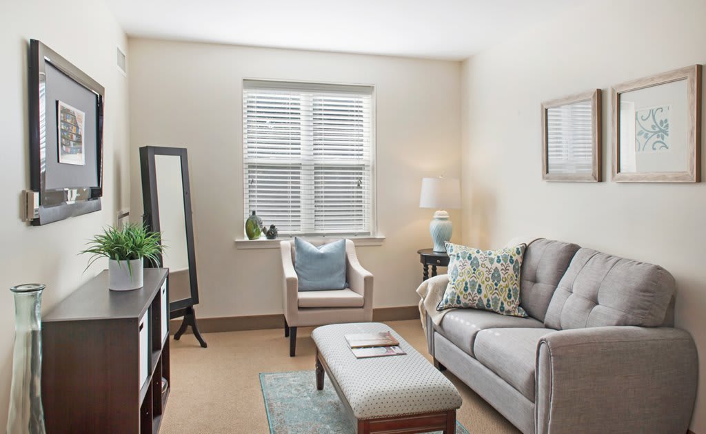 A cozy living room with neutral tones, featuring a sofa, armchair, and an ottoman.