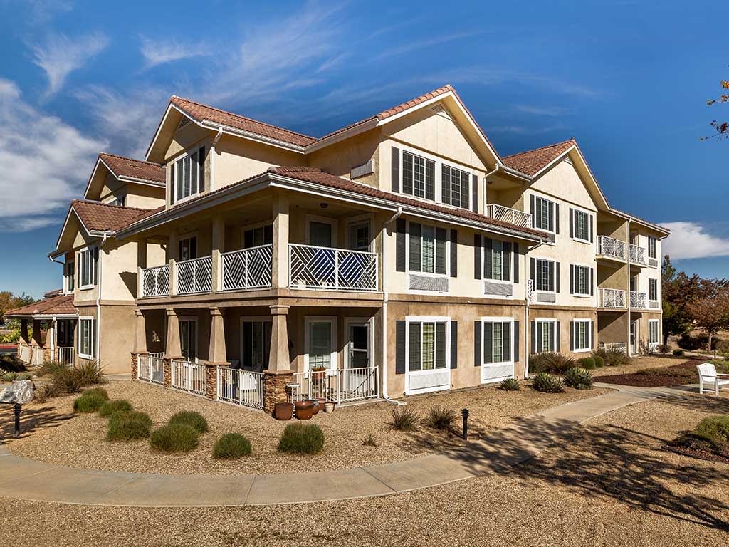 A large two-story residential building with a wraparound porch in a sunny landscape.