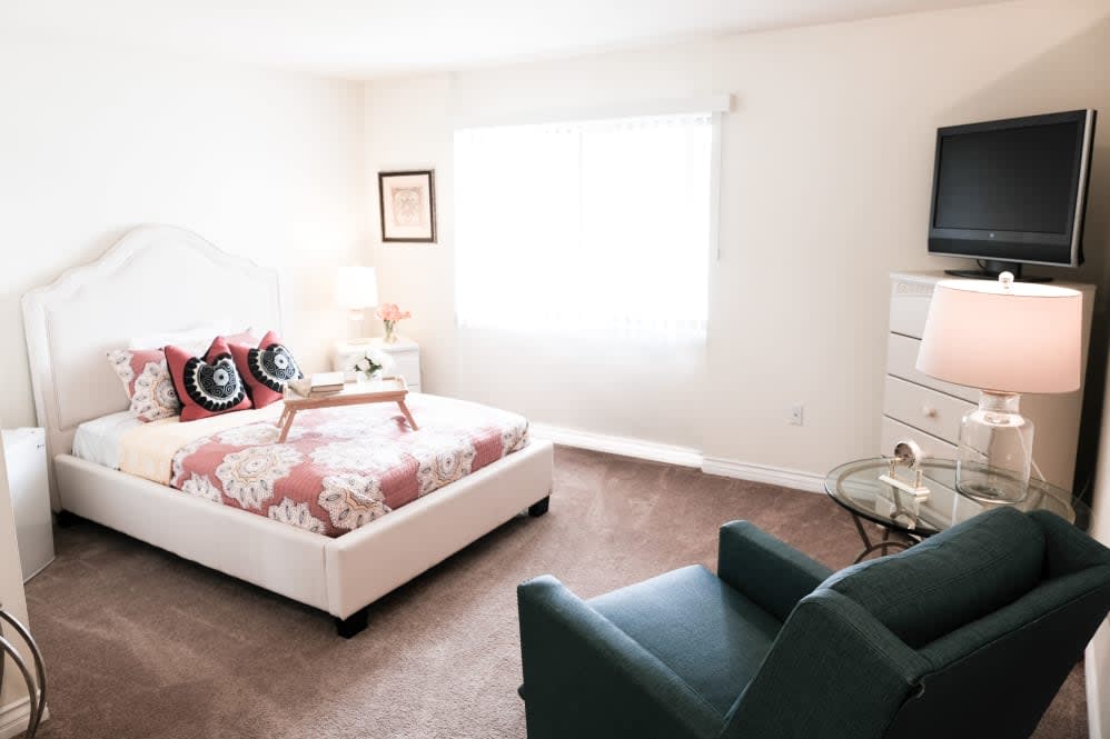 A cozy bedroom with a bed, chair, and soft lighting.