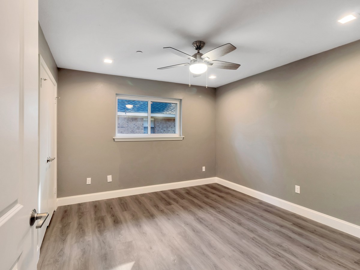 A vacant room with a ceiling fan, wood flooring, and neutral-colored walls.