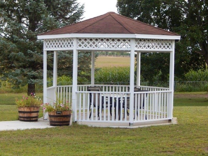 A white wooden gazebo in a garden setting surrounded by greenery.