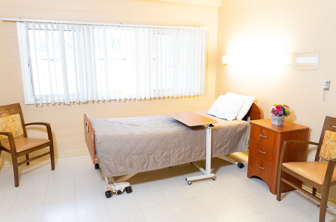 A clean and well-lit hospital room with a single bed and bedside furniture.