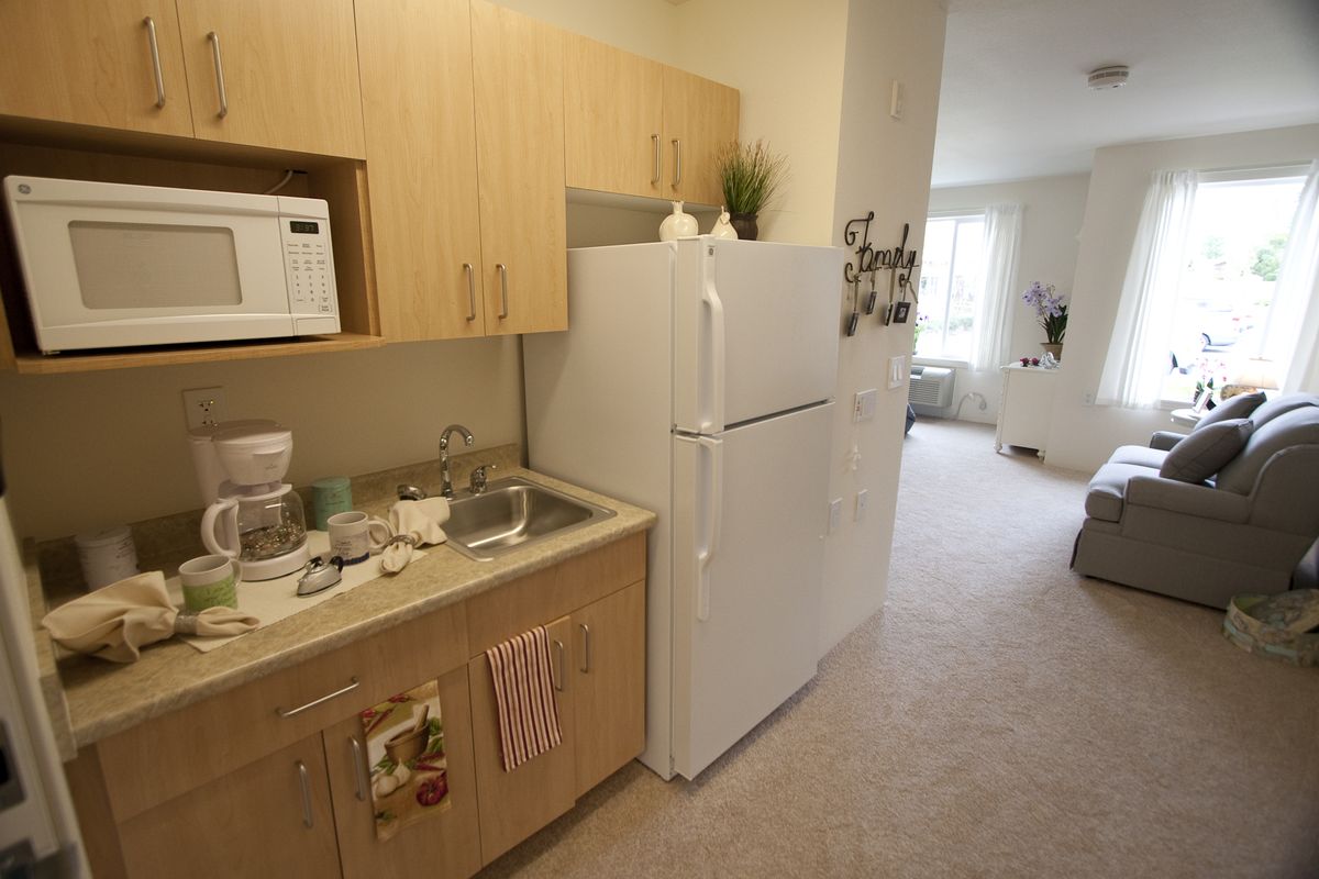 A compact kitchen in an apartment with a microwave, sink, and fridge, leading into a living area.