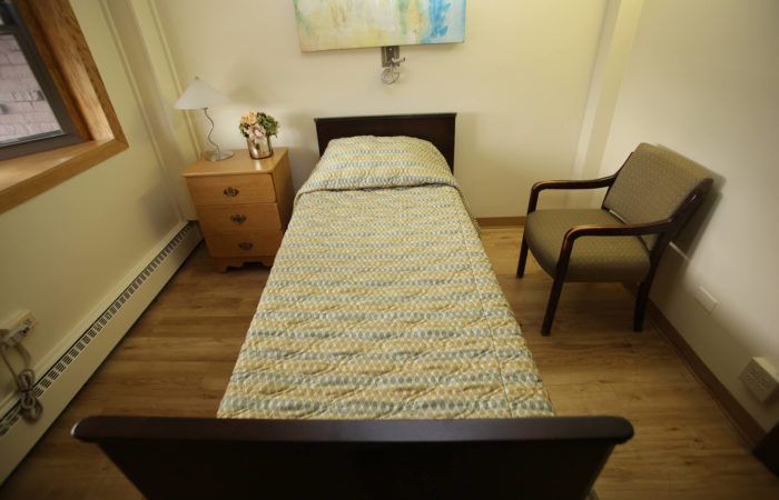 A minimalist bedroom with a single bed, nightstand, and chair.