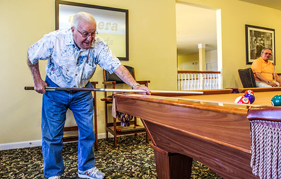 An elderly man playing billiards on a pool table in a recreational room.