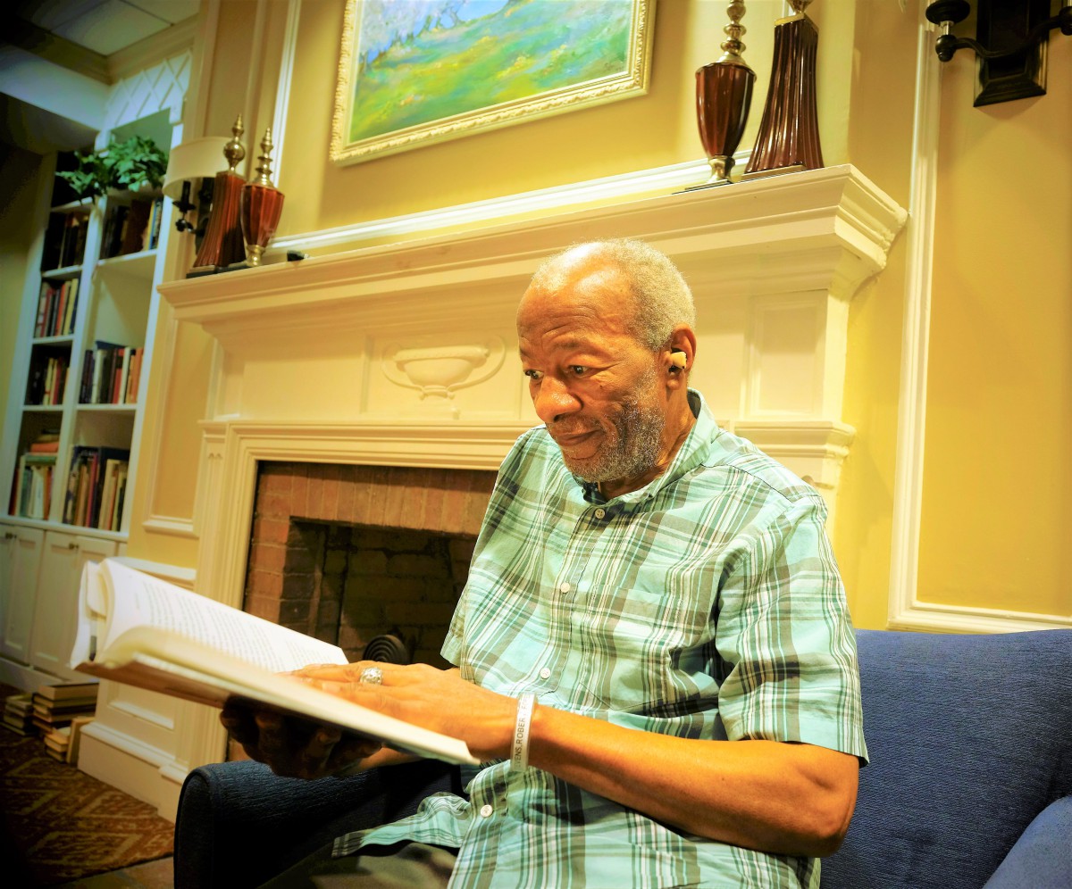 An elderly man enjoying reading a book by the fireplace.