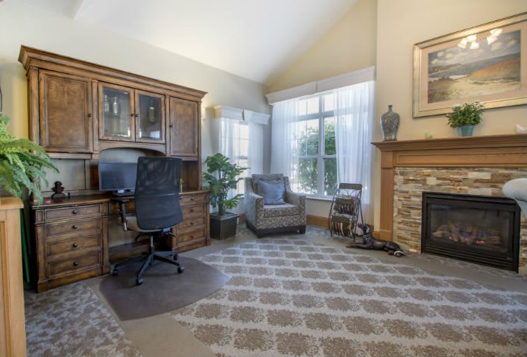 A cozy home office space with a desk, chair, armchair, and fireplace.