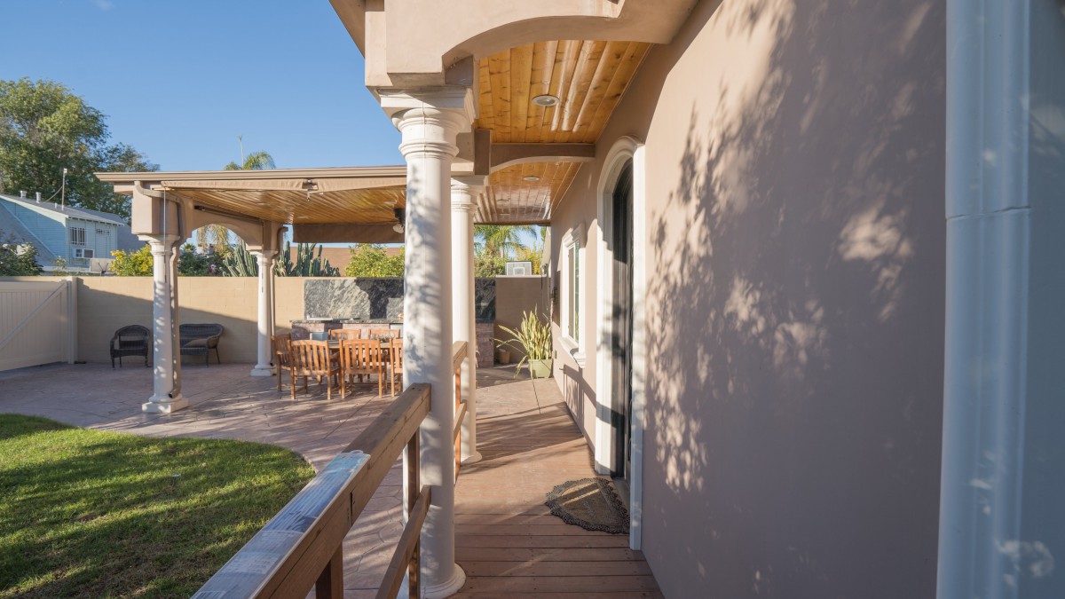 A sunny outdoor patio with a wooden deck, columns, and seating area.