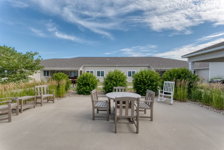 A peaceful outdoor patio area with wooden furniture, surrounded by greenery under a partly cloudy sky.