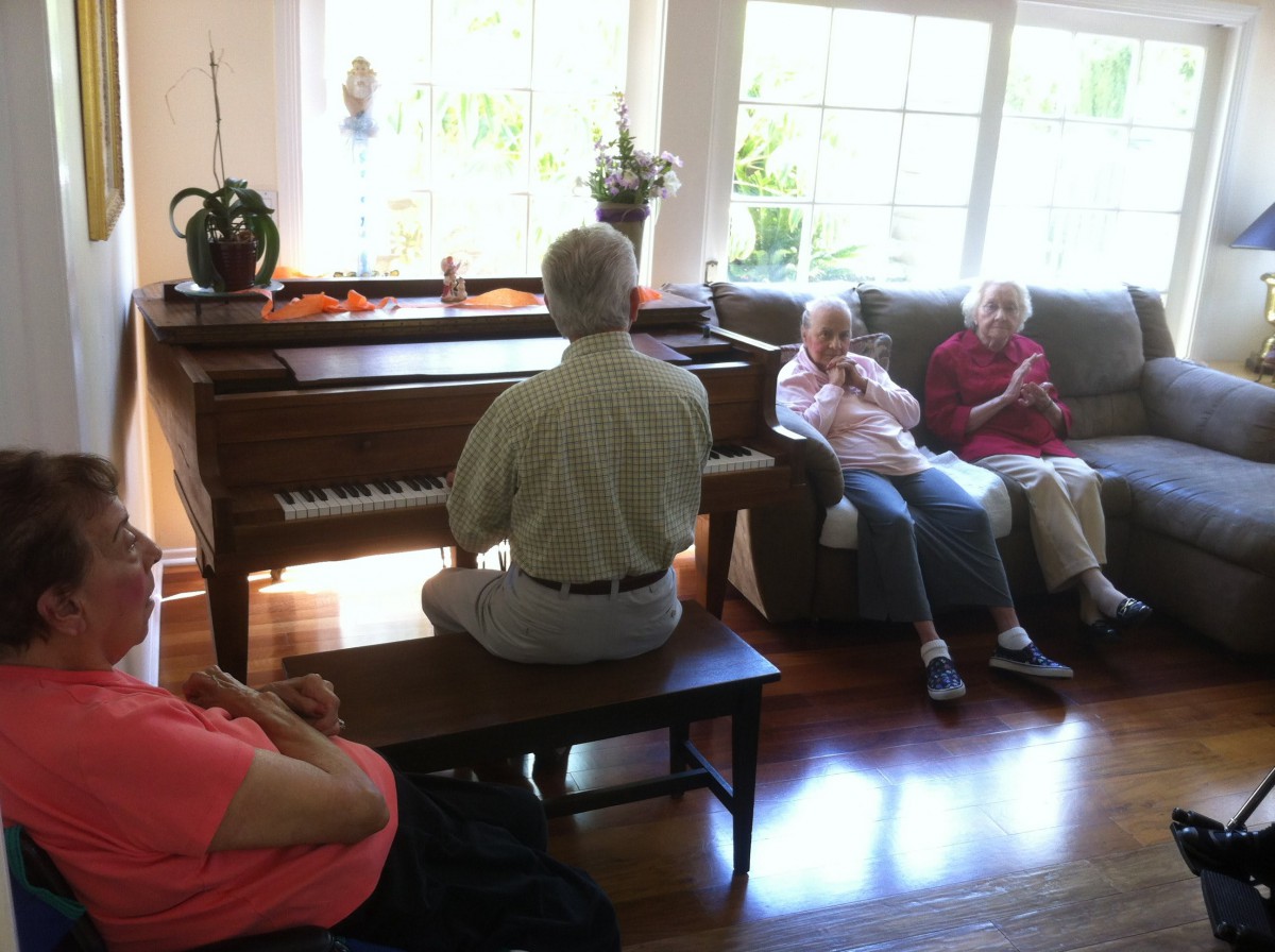 A person playing piano in a living room while others are seated and listening.
