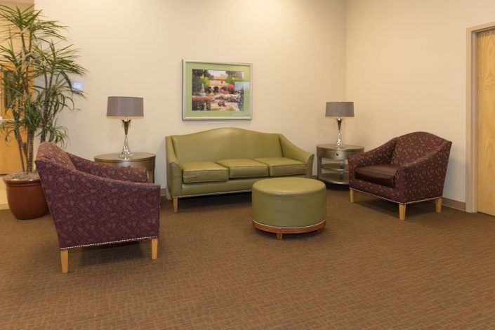 A cozy waiting room with a sofa, chairs, lamps, and a central round ottoman.