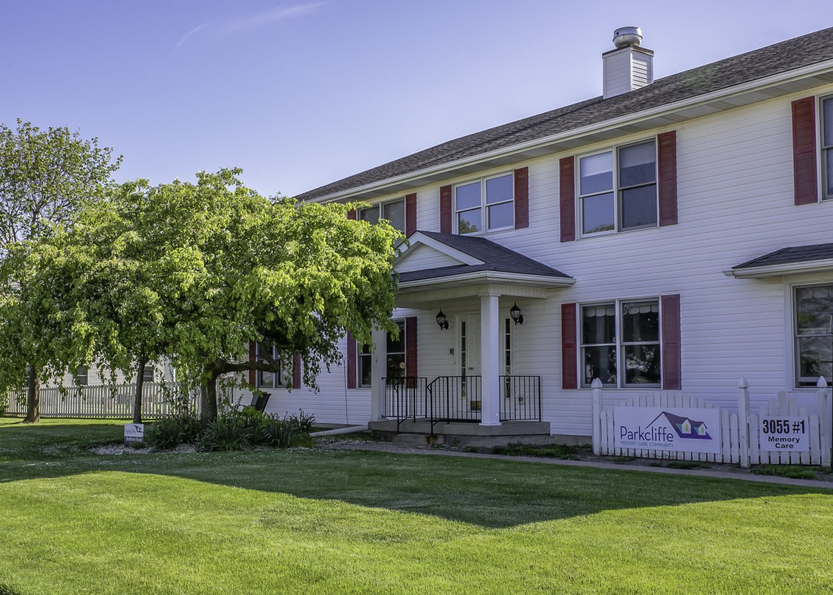 A two-story house with a well-maintained front yard and trees on a sunny day.