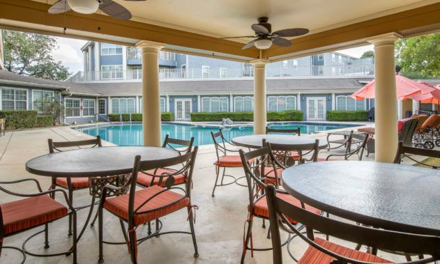 A covered patio with tables and chairs overlooks a swimming pool.
