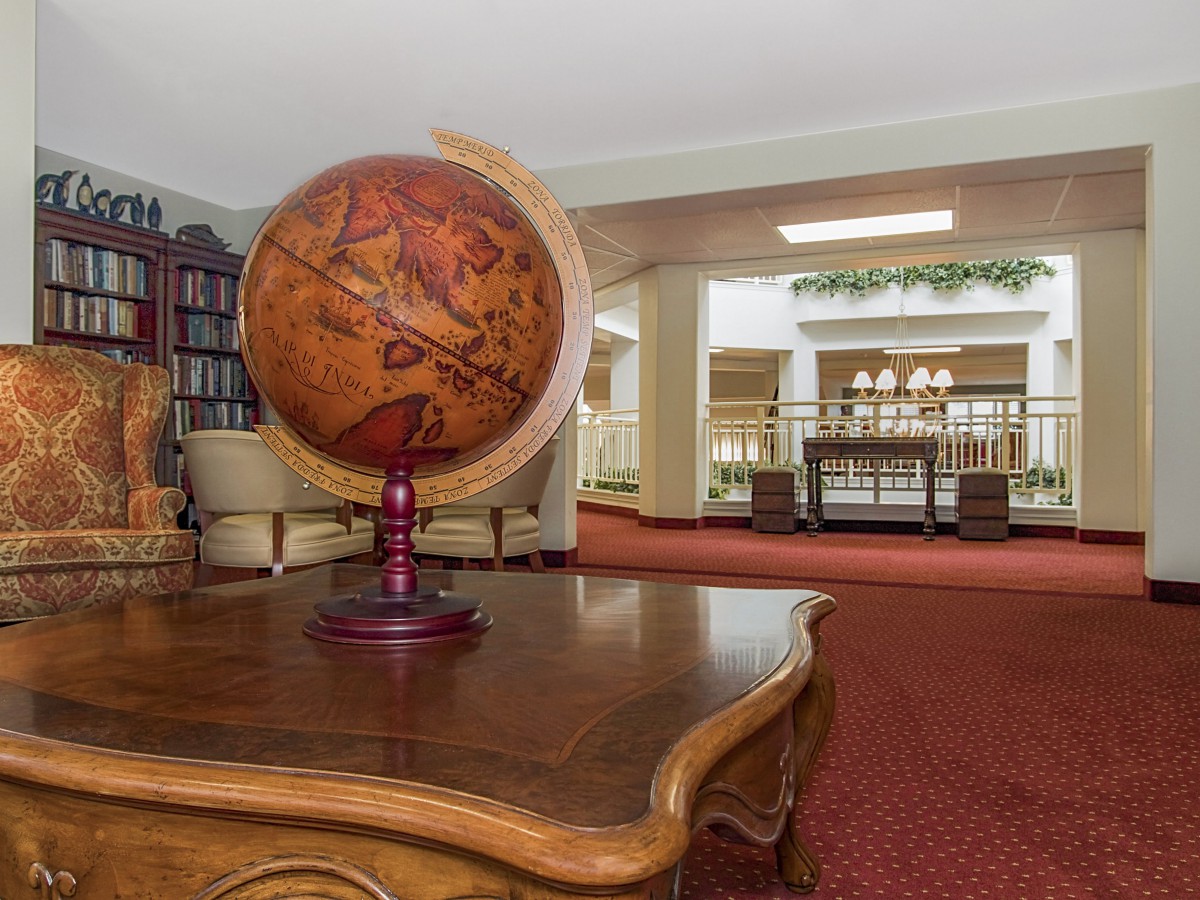 A vintage globe sits on a wooden table in a cozy library setting with bookshelves and classic decor.