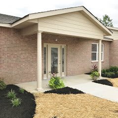 A brick house with a front entrance featuring columns and landscaping.