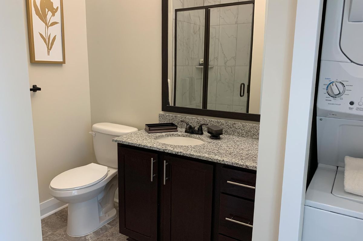 A modern bathroom with a granite countertop, dark wood cabinetry, and a shower with glass doors.