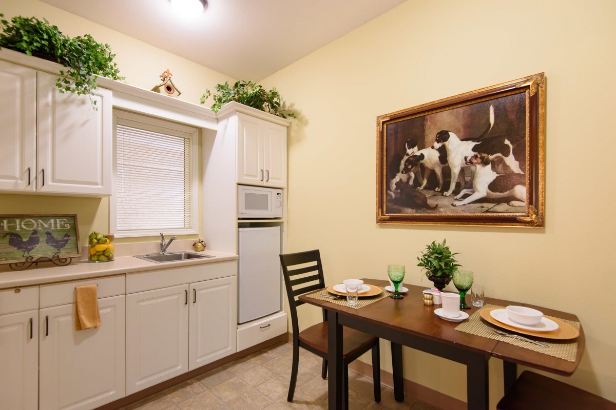 A cozy kitchen with a dining area featuring a small table set for two and decorated with greenery and framed artwork on the wall.